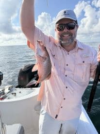 Angler proudly displaying a freshly caught Snapper while fishing on a boat in open waters.