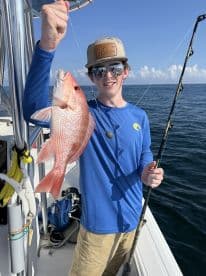 A young angler proudly displaying a vibrant Red Snapper while fishing offshore, showcasing a sunny day on the water.
