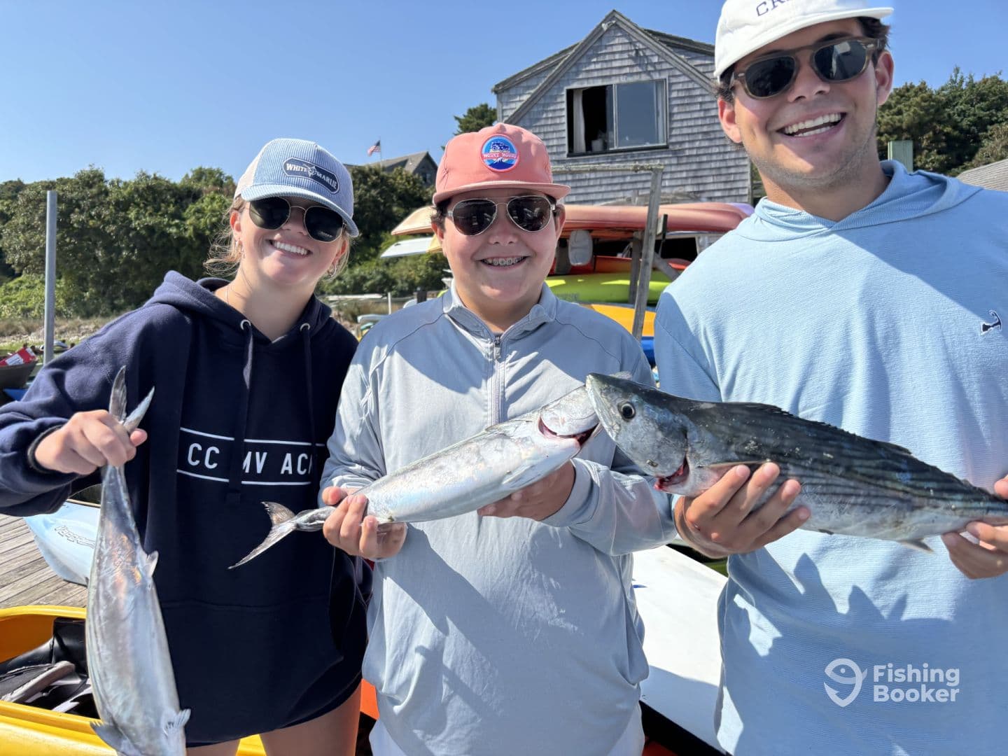 Three young anglers proudly displaying their catch of striped bass and mackerel at the dock, enjoying a sunny day on the water.