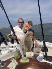 A proud moment on the boat as a young angler holds up a Flounder, accompanied by an adult, showcasing their catch during a fishing trip.