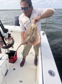 An angler proudly displays a large stingray while fishing on a boat, showcasing the excitement of a successful catch.