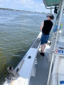 A young angler is actively reeling in a fish from the side of a boat in a calm water setting, showcasing the excitement of fishing.