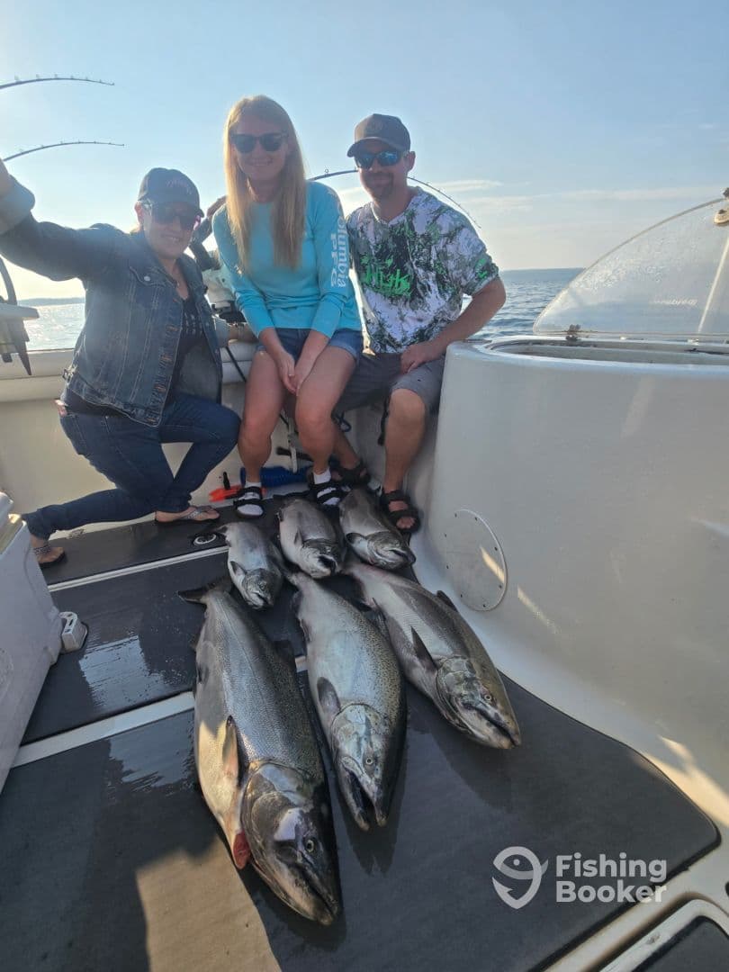 Three anglers posing on a boat with a catch of large Salmon after a successful fishing trip.