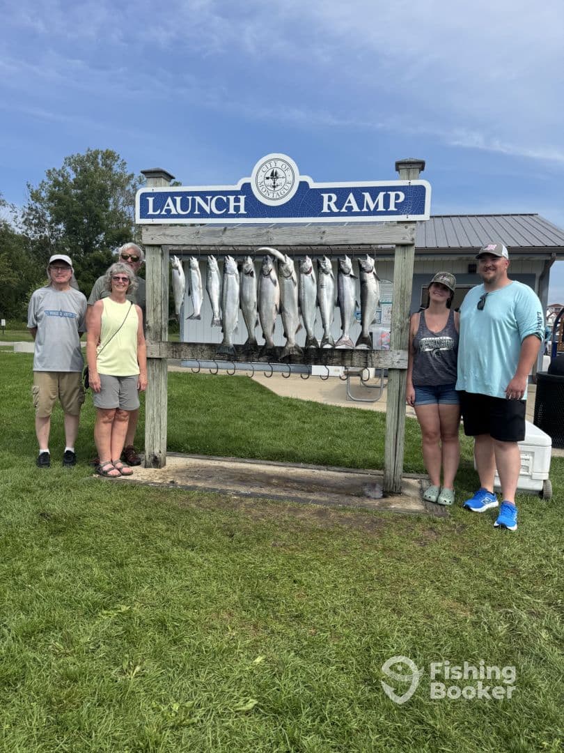 A group of anglers proudly posing in front of a catch board displaying multiple fish at a launch ramp, showcasing their successful fishing trip.