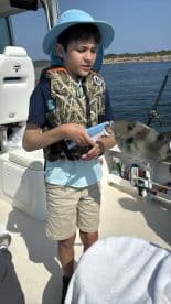 A young angler holding a fish while on a boat, enjoying a day of fishing in a scenic waterway.