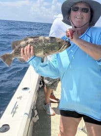An angler proudly displaying a large Grouper while fishing offshore, showcasing a sunny day on the water.
