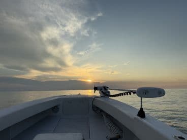A serene view from the helm of a fishing boat at sunrise, showcasing calm waters and a beautiful sky.