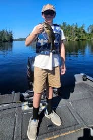 A young angler proudly displaying a smallmouth bass while fishing from a boat in a serene lake setting.