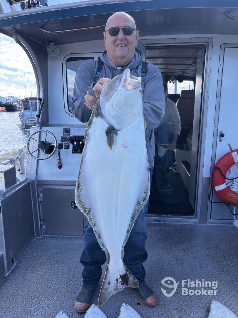 An angler proudly displaying a large Halibut aboard a fishing charter, showcasing a successful day on the water.