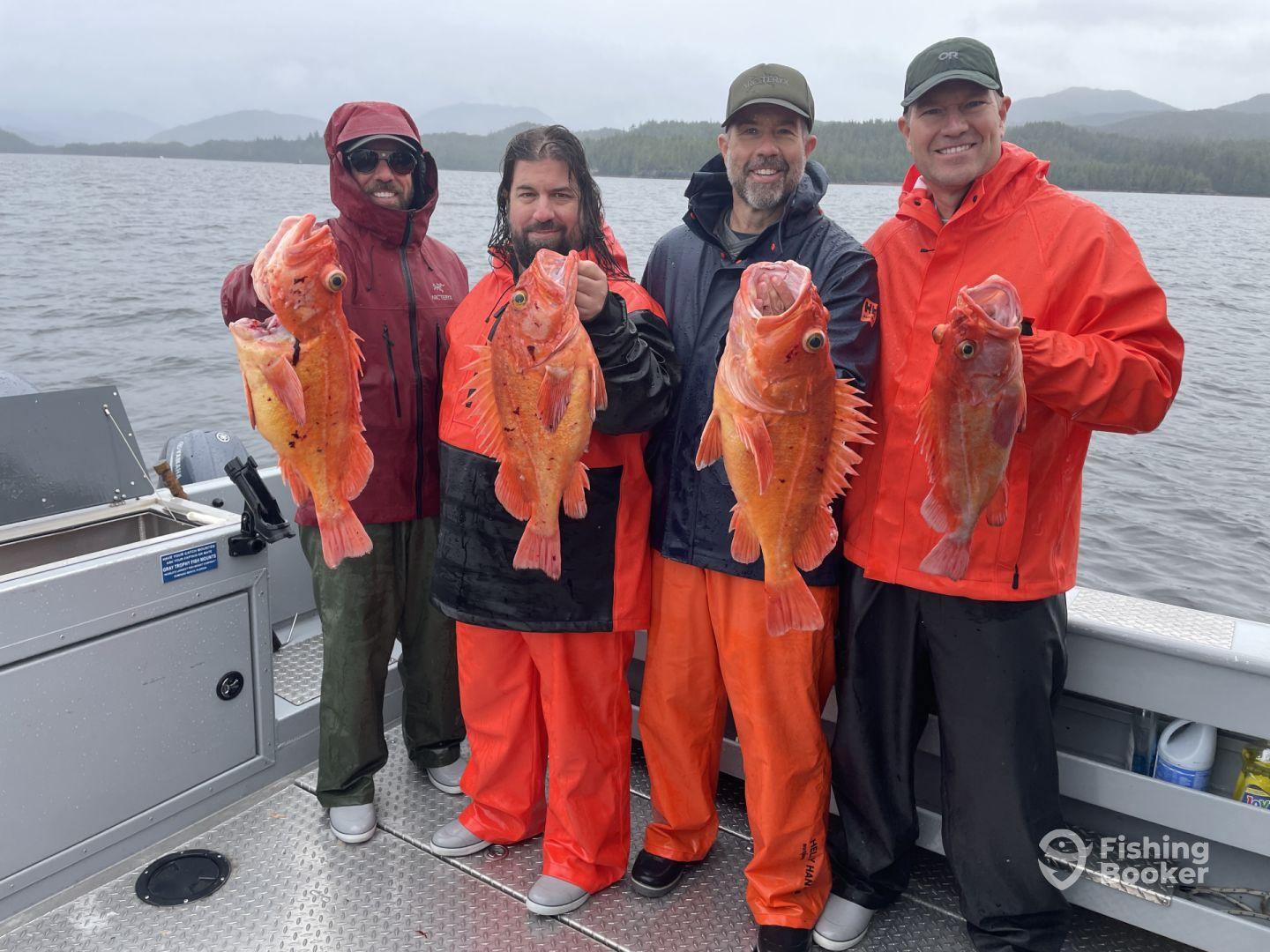 Four anglers proudly displaying their catch of bright orange Rockfish while fishing in rainy conditions on a charter boat.