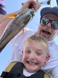 A joyful young angler and an adult proudly displaying a large fish while enjoying a day out on the water.