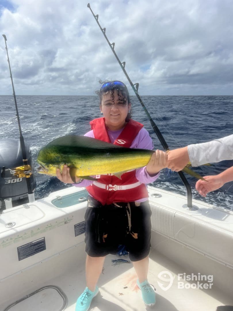 A young angler proudly displaying a vibrant Mahi Mahi while fishing on a boat in open waters.