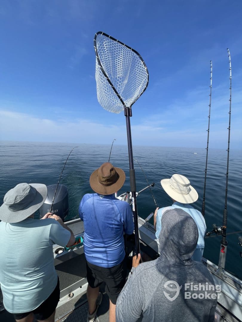 Group of anglers actively fishing on a calm day, with rods in hand and a net ready for landing the catch.