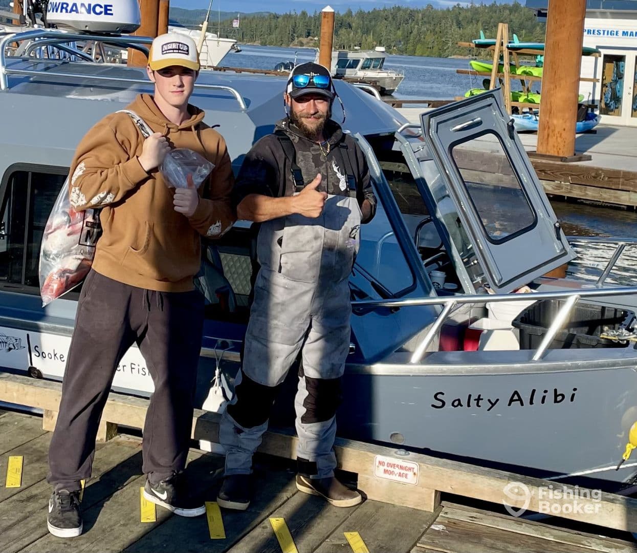 A young angler and a guide proudly displaying their catch at the dock next to the 'Salty Alibi' boat after a successful fishing trip.