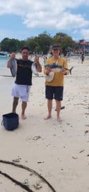 Two anglers proudly displaying their catch of fish on a sandy beach after a successful fishing trip.