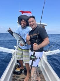 Two anglers celebrating a successful catch of a large fish while fishing on a boat in open waters.