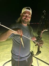 Angler using a bow to catch fish at night, showcasing a unique fishing technique in shallow waters.