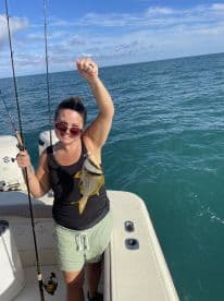 An angler proudly displaying a colorful Yellowtail Snapper while fishing on a boat in clear blue waters.