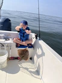 A young angler is reeling in a stingray while fishing on a small boat, showcasing a fun day on the water.