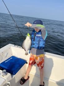 A young angler proudly displaying a Flounder while fishing on a boat, showcasing a sunny day on the water.