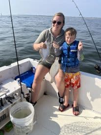 A mother and her young son proudly displaying their catch of Flounder while fishing on a boat, enjoying a sunny day on the water.