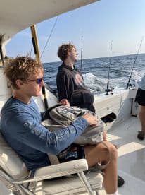 Two young anglers relaxing on the boat while fishing, with rods ready for action in the background.