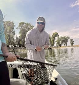 Angler holding a freshly caught fish while fishing from a boat in a scenic lake environment.