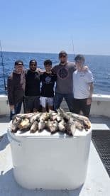 A group of anglers proudly displaying their catch of multiple fish on a fishing charter in open waters.