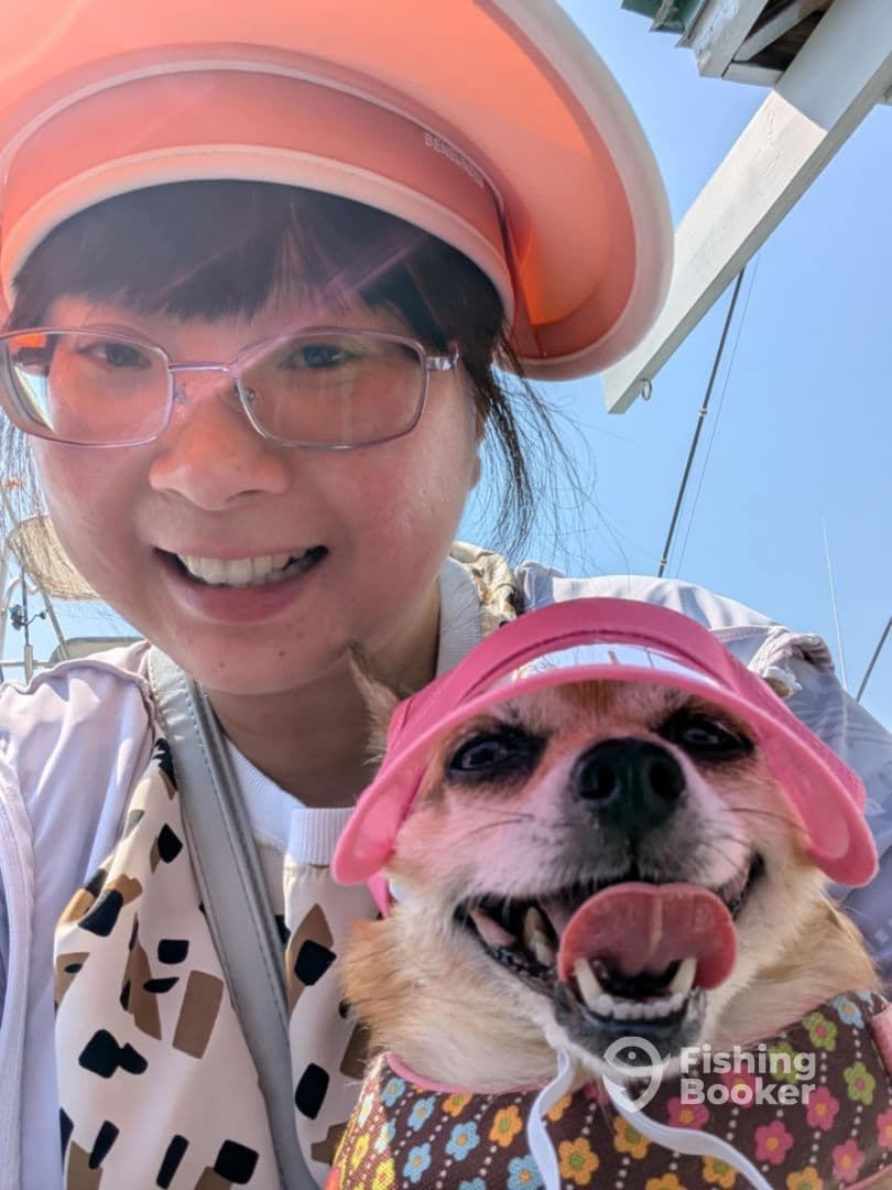 A smiling individual and a dog wearing matching pink visors, enjoying a sunny day on a boat.