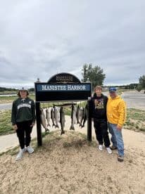 A group of anglers proudly displaying their catch of salmon on a board at Manistee Harbor, showcasing a successful fishing trip.
