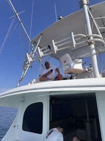A crew member relaxes on the upper deck of a sportfishing boat, showcasing the spacious helm area and clear blue skies.