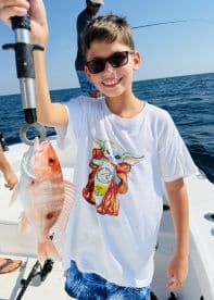 A young angler proudly displaying a freshly caught Snapper while fishing on a sunny day.