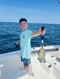 A young angler proudly displaying a freshly caught fish while fishing on a boat in open waters.