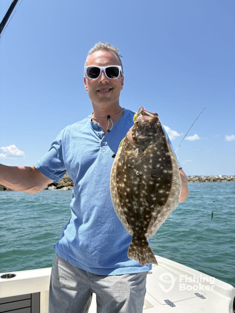 An angler proudly displaying a large Flounder while fishing on a sunny day, showcasing the vibrant blue waters.