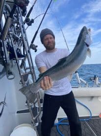 An angler proudly displaying a large Steelhead trout while fishing on a boat, showcasing a successful day on the water.