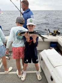 A young angler proudly displaying a caught fish while fishing on a boat, surrounded by friends in a fun, family-friendly atmosphere.