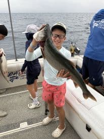 A young angler proudly displaying a large Lake Trout while fishing on a charter boat, surrounded by fellow anglers.