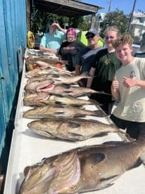 A group of anglers proudly displaying a large catch of Grouper on a catch board after a successful fishing trip.