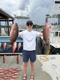 Angler proudly displaying two large Red Snapper at the dock after a successful fishing trip.