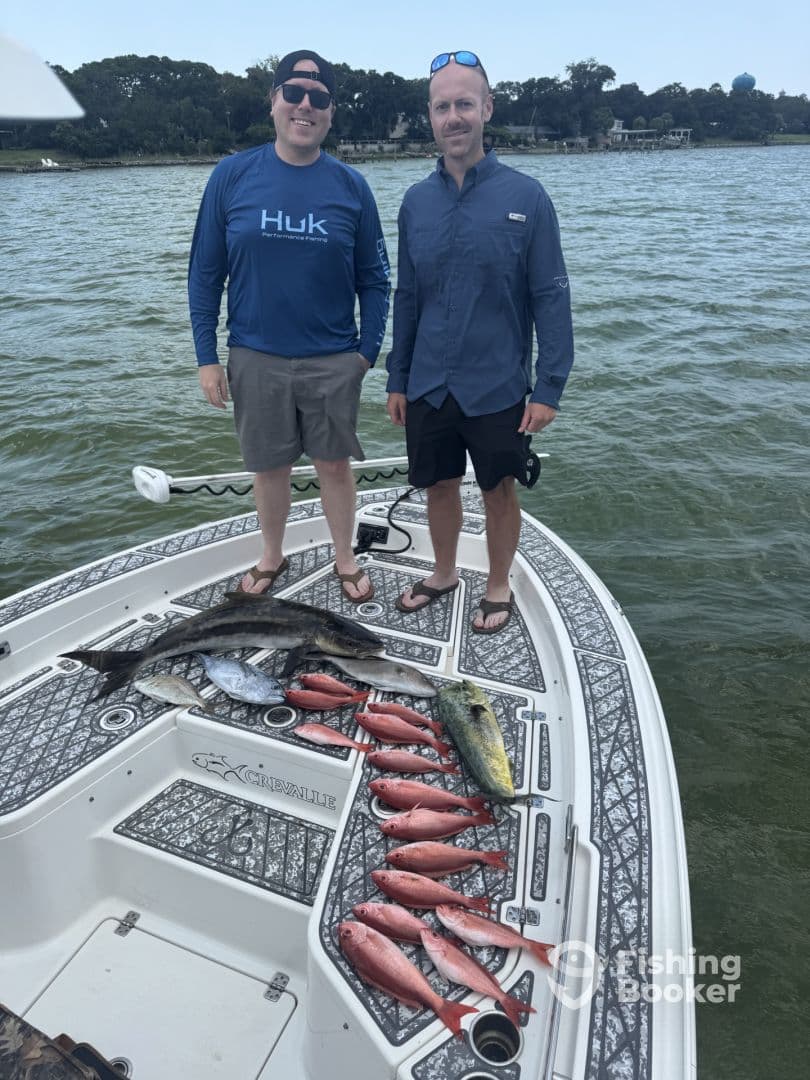 Two anglers proudly displaying a variety of fish, including a large Cobia and several Snapper, on the deck of a Crevalle boat during a fishing trip.