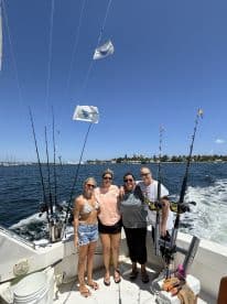 Group of four anglers enjoying a day on a fishing charter, with fishing rods ready for action against a scenic backdrop.