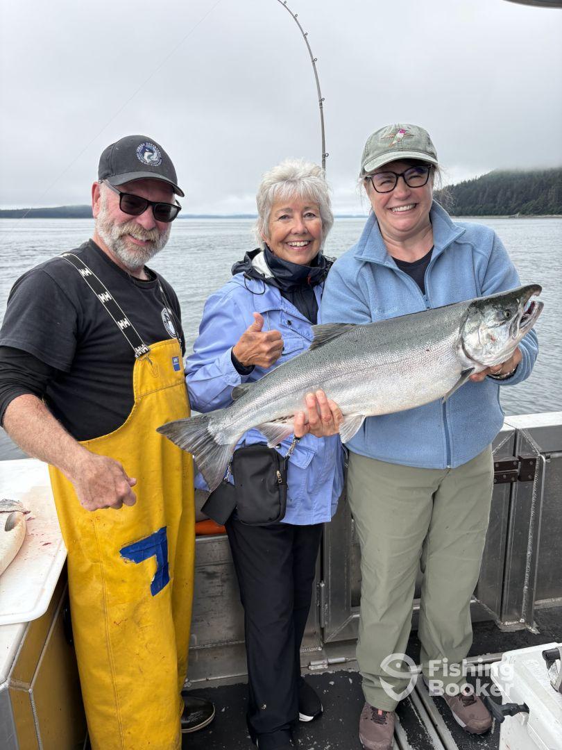 Three anglers proudly displaying a large Silver Salmon on a fishing charter in a scenic coastal environment.