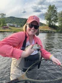 An angler proudly displaying a freshly caught fish while enjoying a scenic day on the river.