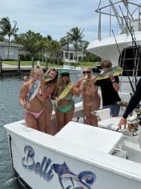 A group of young adults proudly displaying their catch of Mahi Mahi and other fish aboard the Belli, enjoying a sunny day in a coastal marina.