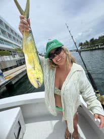Angler proudly displaying a vibrant Mahi Mahi while aboard a fishing boat, with a scenic waterfront in the background.