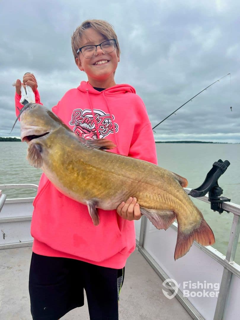 A young angler proudly displaying a large catfish while fishing on a boat, showcasing the excitement of a successful catch.