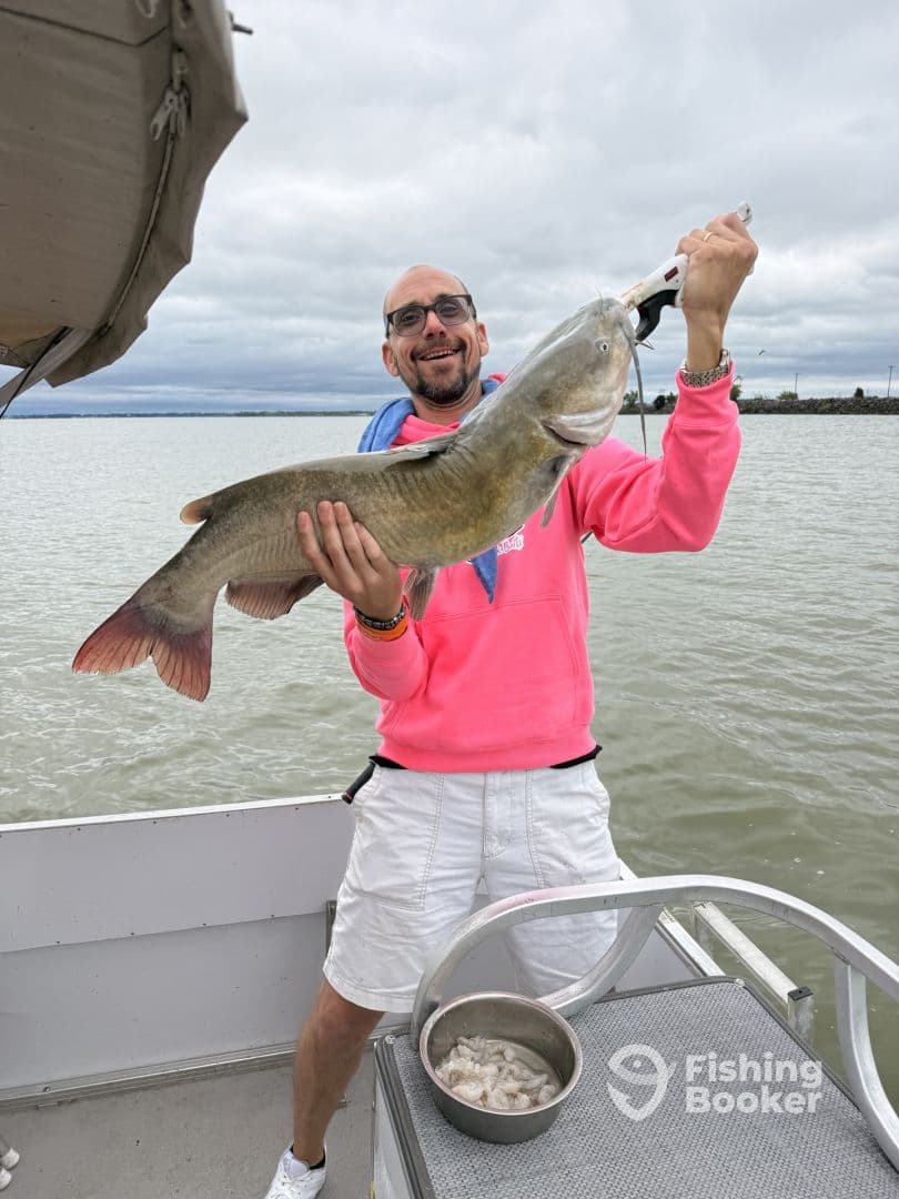 An angler proudly displaying a large catfish while fishing from a boat, showcasing a successful catch on a cloudy day.