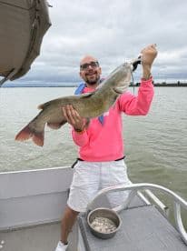 An angler proudly displaying a large catfish while fishing from a boat, showcasing a successful catch on a cloudy day.