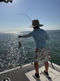 A young angler is reeling in a fish while fishing on a sunny day, showcasing the excitement of the catch in a vibrant fishing environment.