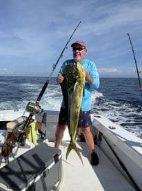An angler proudly displaying a large Mahi Mahi while aboard a fishing boat in open waters.